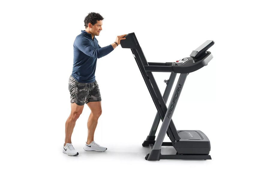 Man in navy shirt and gray shorts using black ProForm treadmill with digital display on white background