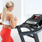 Woman in white sports bra and red leggings running on black ProForm treadmill with touchscreen display