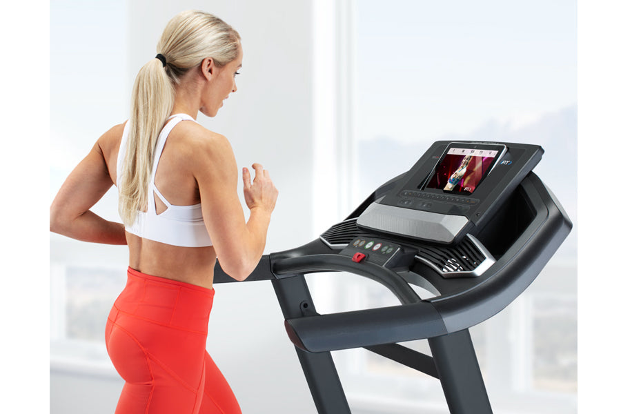 Woman in white sports bra and red leggings running on black ProForm treadmill with touchscreen display