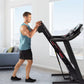 Man in teal tank top using black ProForm treadmill with digital display in bright room with windows