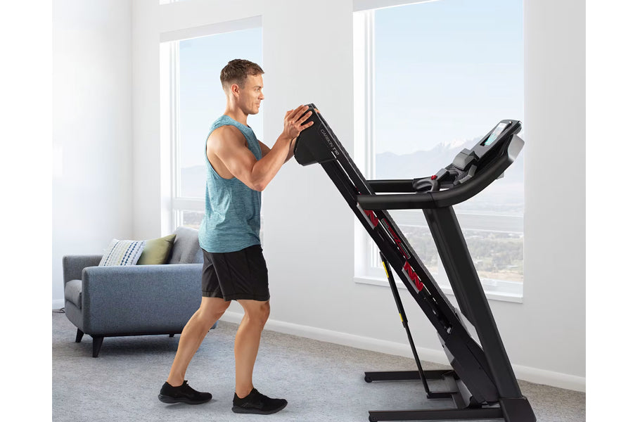 Man in teal tank top using black ProForm treadmill with digital display in bright room with windows
