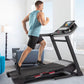 Man wearing blue heathered tank top and black shorts running on black ProForm treadmill with digital display in modern home i