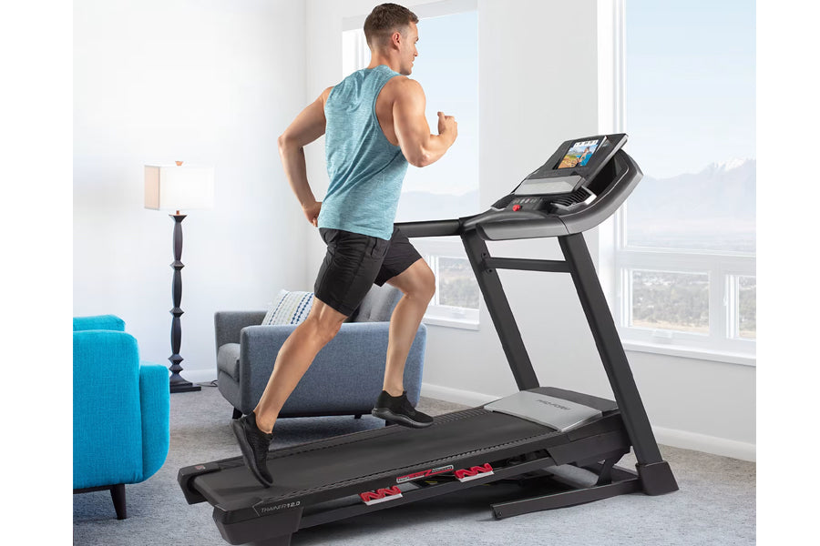 Man wearing blue heathered tank top and black shorts running on black ProForm treadmill with digital display in modern home i