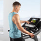 Man wearing light blue heathered sleeveless tank top using black ProForm treadmill with digital display in bright room
