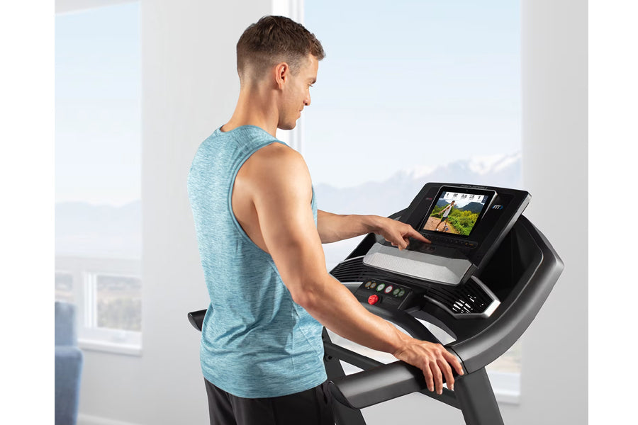Man wearing light blue heathered sleeveless tank top using black ProForm treadmill with digital display in bright room