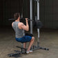 Man using Body-Solid Pro Lat Machine with gray tank top and blue shorts in gym setting