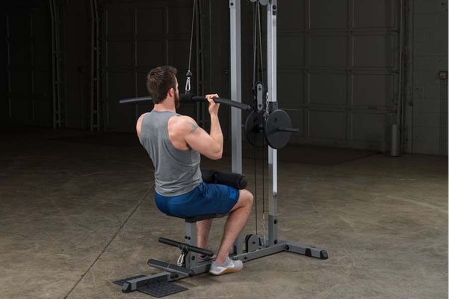 Man using Body-Solid Pro Lat Machine with gray tank top and blue shorts in gym setting