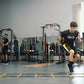 Athlete performing footwork drill with yellow and black agility ladder on gym floor, wearing SKLZ branded gear