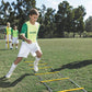 Boy performing agility drill on yellow and black speed ladder on soccer field with coach and teammates in background