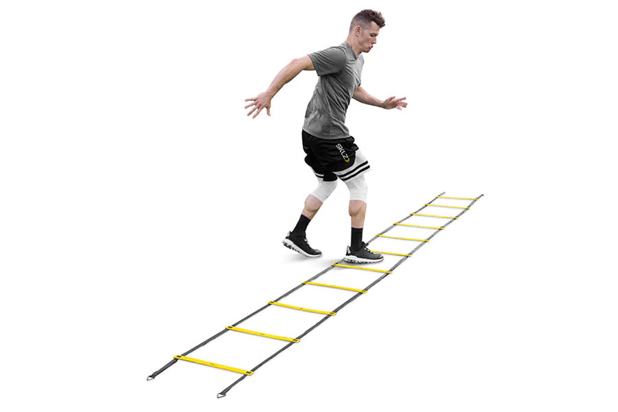Man in gray t-shirt and black shorts training on yellow and gray agility ladder on white background