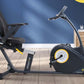 Black and yellow recumbent exercise bike with padded seat, positioned in modern home gym setting with blue wall
