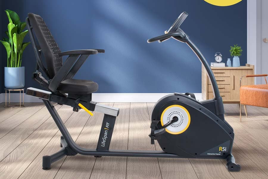 Black and yellow recumbent exercise bike with padded seat, positioned in modern home gym setting with blue wall
