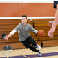 Man in gray t-shirt and black pants dribbling basketball on gym court, demonstrating ball handling during practice