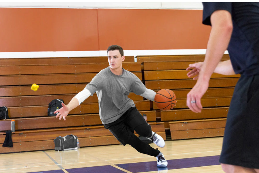 Man in gray t-shirt and black pants dribbling basketball on gym court, demonstrating ball handling during practice