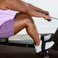 Woman in lavender tank top and purple shorts using black indoor rowing machine