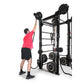 Man in pink shirt performing overhead dumbbell press on black Ropeflex RX2100 functional trainer with weight plates