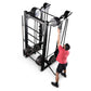 Black steel cable machine with dual pulleys and weighted stack, man in pink shirt demonstrating overhead pull exercise