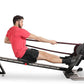 Man in red t-shirt and black shorts using black Ropeflex RX3200 rowing machine with rope handles on white background