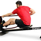 Man in red t-shirt and black shorts using black Ropeflex rowing machine with rope on white background