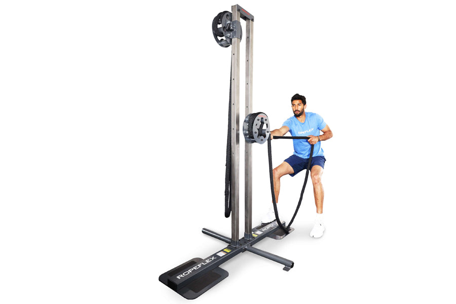 Man in blue shirt using tall black and gray upright rope trainer machine with weighted pulley system on white background