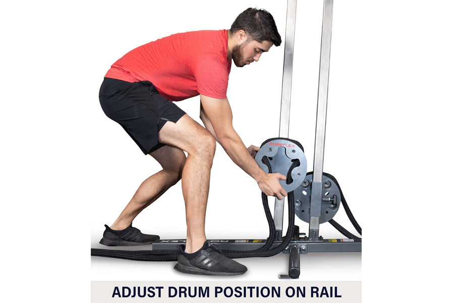Man in red shirt and black shorts using gray Ropeflex RX1500 rope trainer, adjusting drum position on rail