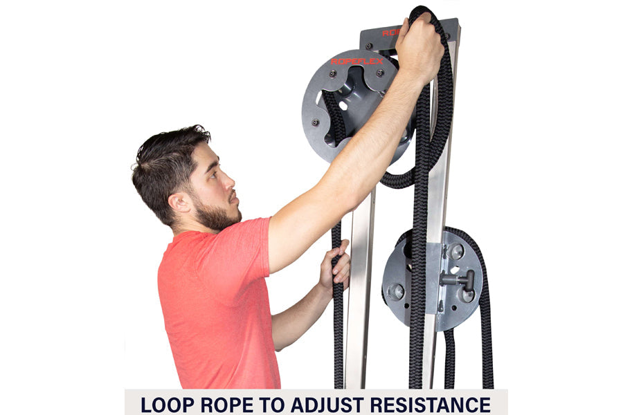 Man in coral shirt using gray and black upright rope trainer with dual pulley system and loop rope handles