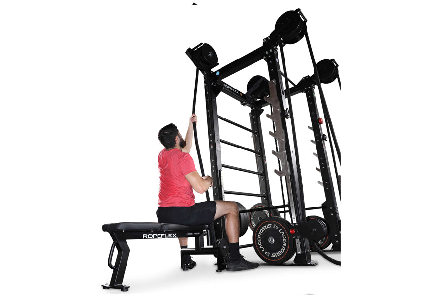 Man wearing pink shirt using RopeFlex RX2100 black rope trainer machine with bench seat on white background
