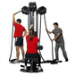 Black and gray multi-station rope training machine with two black rope handles, used by three people in workout attire on whi