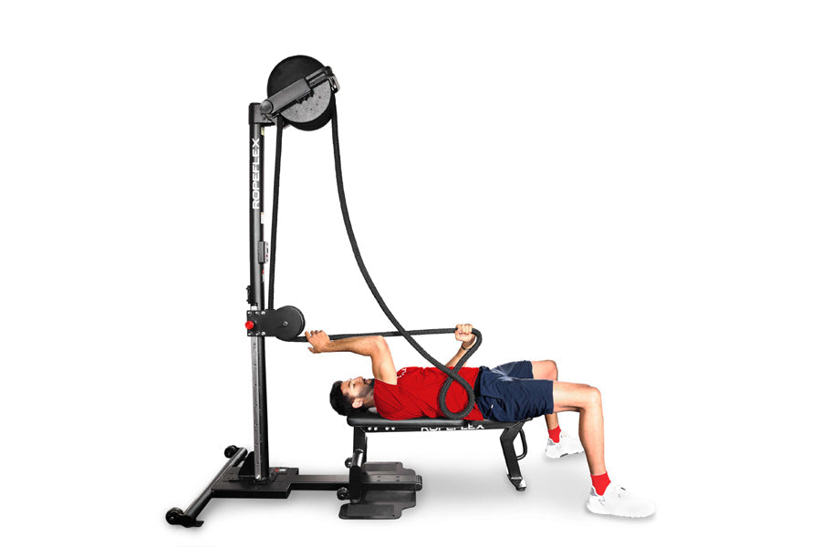 Male model in red shirt and navy shorts using black Ropeflex RX2500 upright rope trainer with adjustable seat and overhead pu