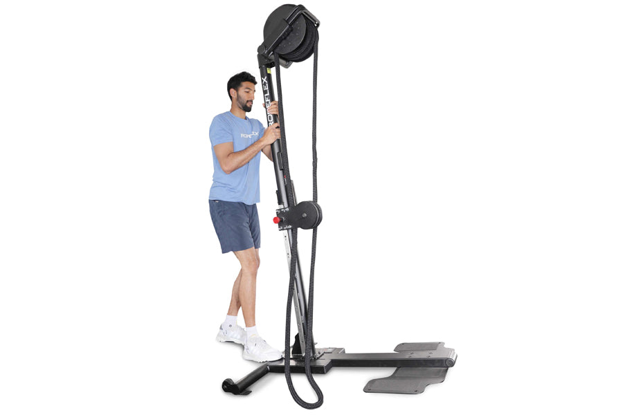 Man in blue t-shirt and navy shorts using black upright rope trainer with overhead pulley system on white background