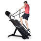 Man in pink t-shirt and black shorts using black Ropeflex RX4400 rope climbing machine against white background