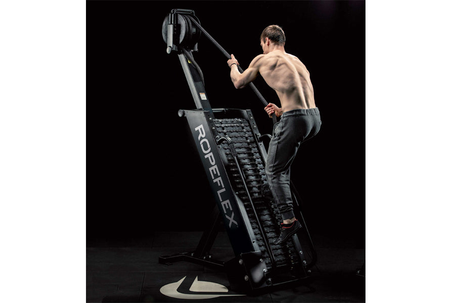 Shirtless man climbing black Ropeflex RX4400 rope trainer with overhead rope attachment on black background