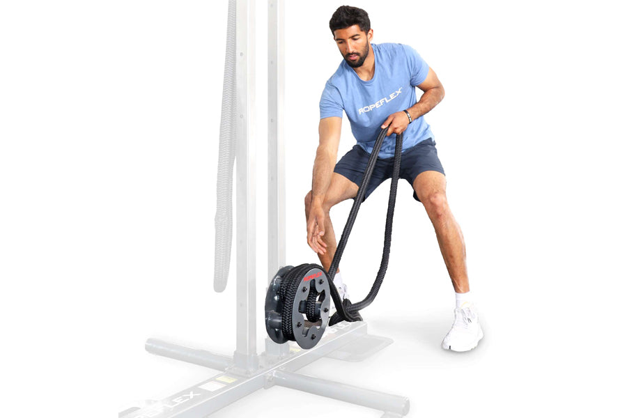 Man using black rope drum attachment on white frame, wearing blue graphic tee and navy shorts