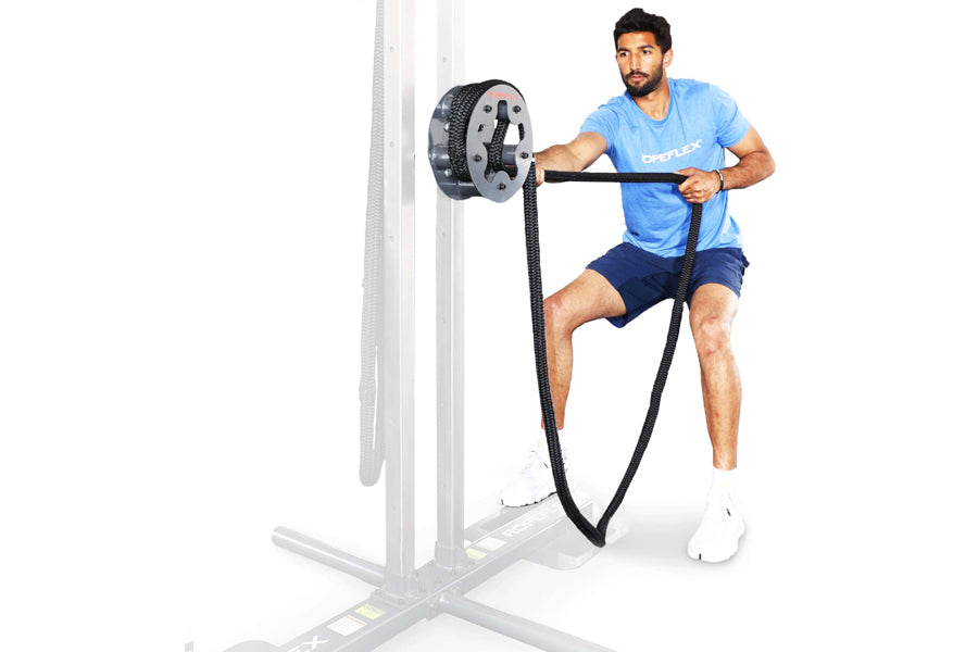 Man in blue t-shirt using black rope attached to gray mechanical drum attachment on wall-mounted frame