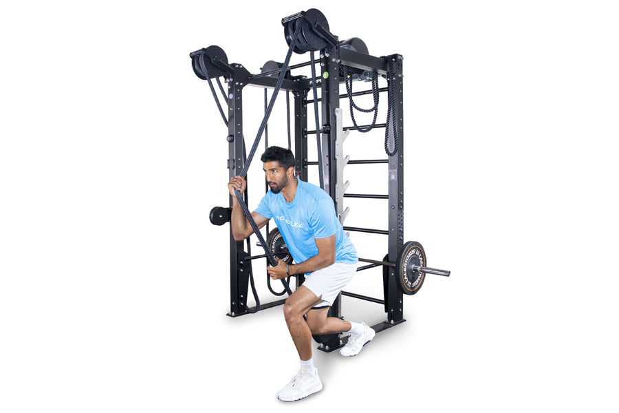 Man in blue shirt using black cable machine with dual pulleys and rope attachments on white background