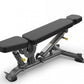 TRUE SF-1000 adjustable weight bench with black padded seat and backrest, gray metal frame, and leg attachment on white backg