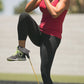 Maroon sleeveless athletic tank top with black capri leggings and yellow resistance band, worn by model jumping outdoors