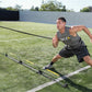 Male athlete performing sled push drill on grass field wearing gray tank top and black shorts with resistance harness attache