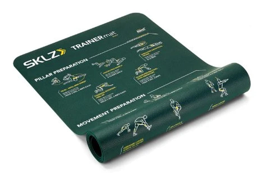 Dark green SKLZ Trainer Mat with white and gold instructional exercise diagrams printed across surface, partially rolled to s