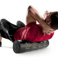Man using black foam roller for back massage while lying on white background, wearing red shirt and black shorts