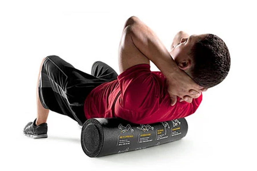 Man using black foam roller for back massage while lying on white background, wearing red shirt and black shorts