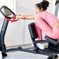 Woman in pink athletic wear using stationary stretch machine with digital display in home gym setting