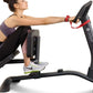 Woman using black LifeSpan stationary bike with red resistance band for stretching, worn by model on white background