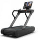 TRUE Stryker Slat Treadmill with black and gray frame, dual handles, and touchscreen display showing workout content on white