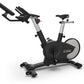 TRUE Surge indoor stationary exercise bike with black seat and handlebars, silver frame accents, and gray flywheel, on white 