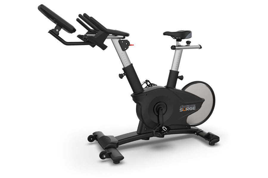 TRUE Surge indoor stationary exercise bike with black seat and handlebars, silver frame accents, and gray flywheel, on white 