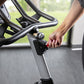 Person adjusting red resistance knob on black and gray stationary exercise bike with curved handlebars