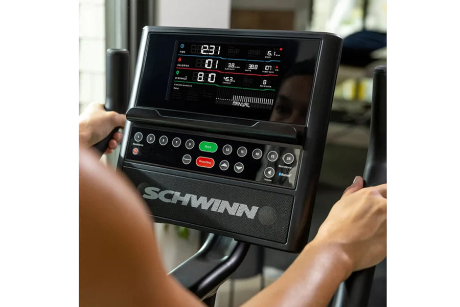 Schwinn 190 upright exercise bike console with digital display showing metrics, held by user's hands during indoor workout
