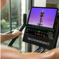 Person holding handlebar of Schwinn 190 upright exercise bike displaying screen with cyclist on purple background