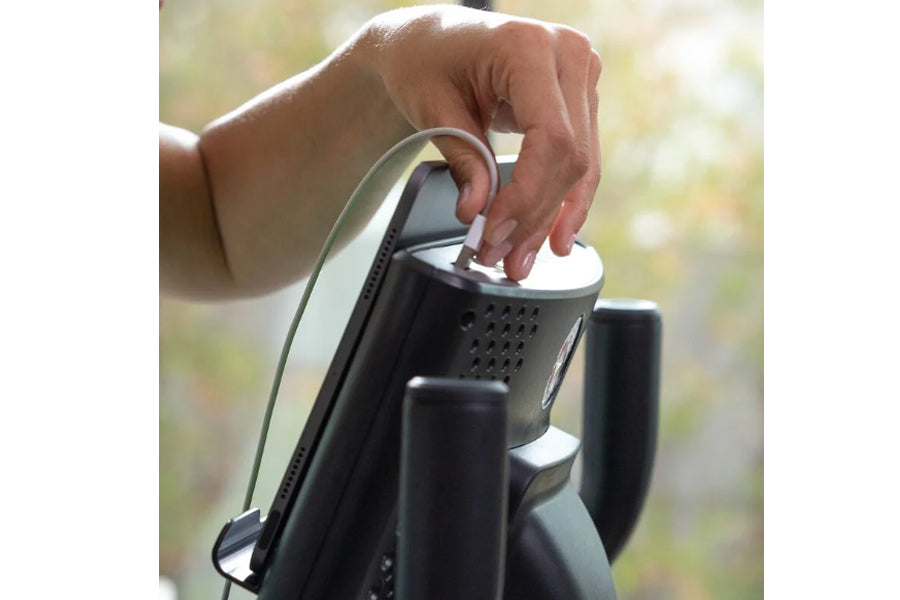 Hand adjusting white and black upright exercise bike seat held outdoors